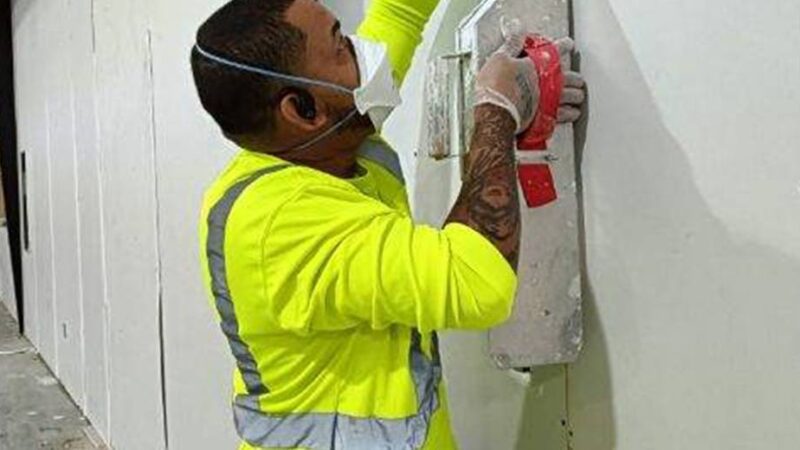 Worker sanding wall with protective gear